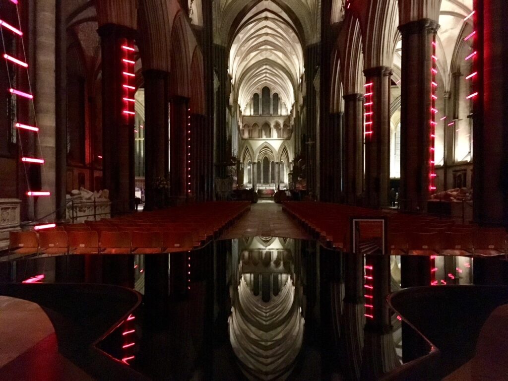 ladders of light installation featuring neon red ladders up he walls of the cathedral reflected in the font
